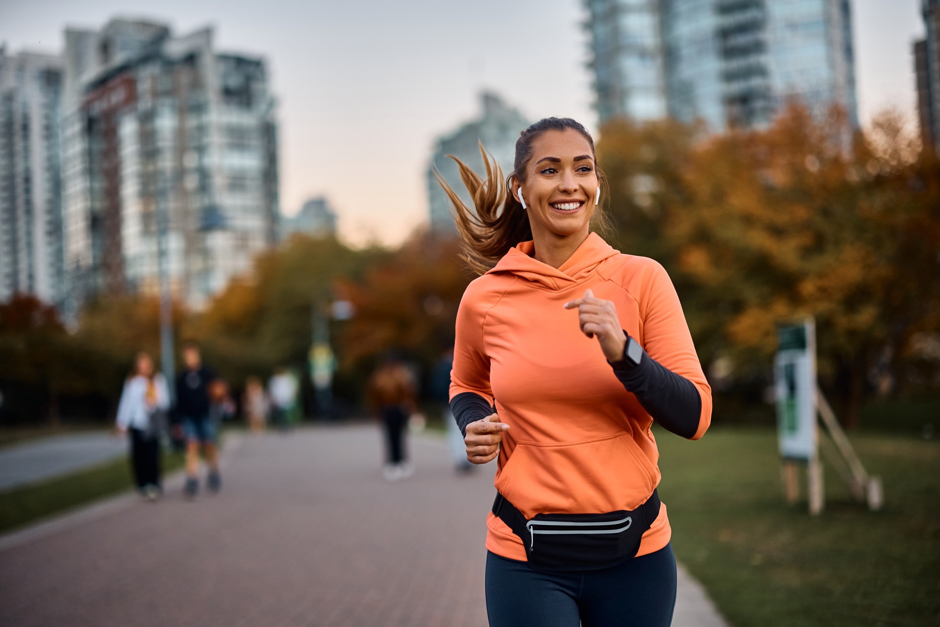 Happy sportswoman with earbuds running in the park.